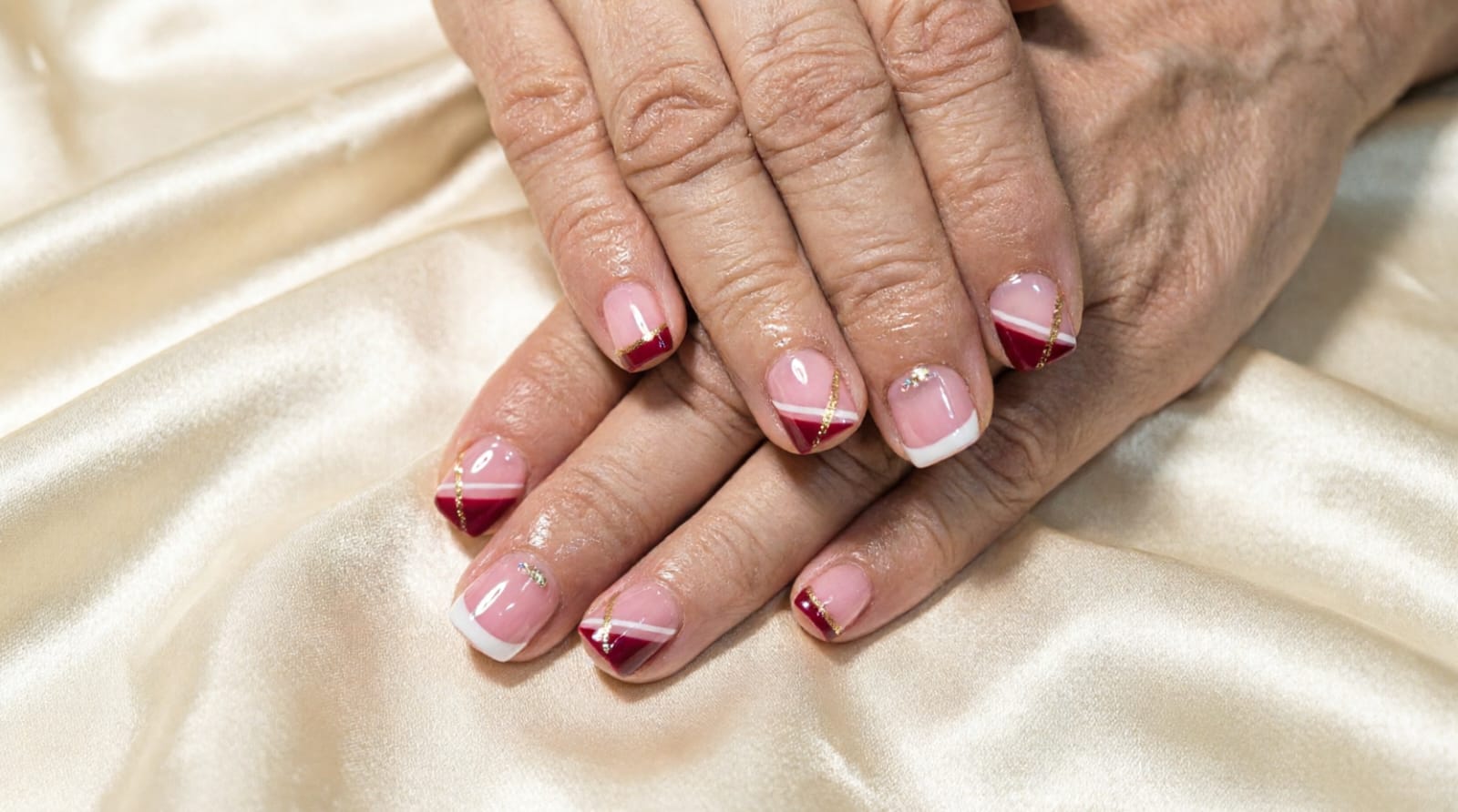 Manicura francesa vino con líneas doradas sobre satén
